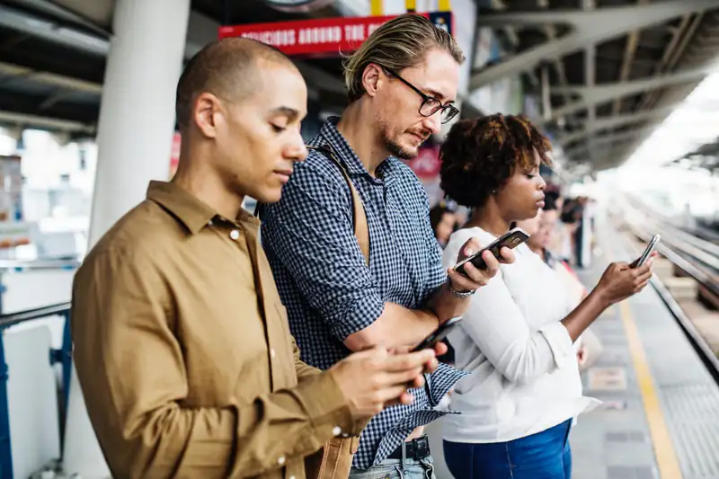 Commuters on a train platform looking at their smartphones